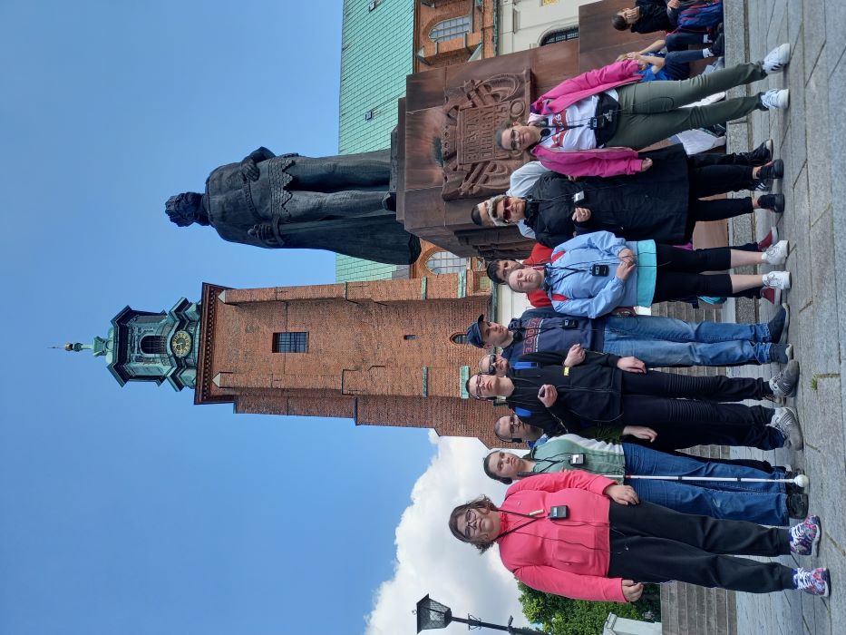 Grupa uczniów z opiekunami przed Katerdrą w Gnieżnie, za nimi pomnik Bolesława Chrobrego