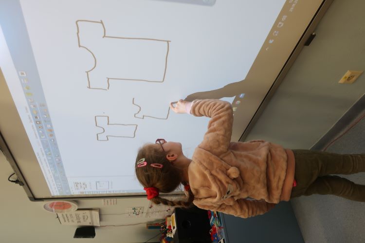 Dziewczynka na tablicy rysuje kształt koszulki