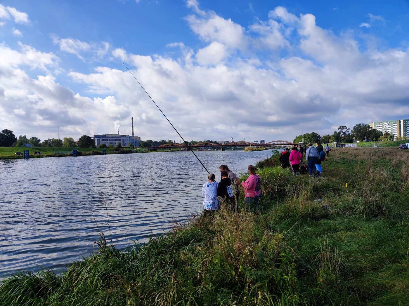 Ogólny widok na rzekę Odrę i uczestników zawodów wędkarskich siedzących z wędkami nad brzegiem rzeki