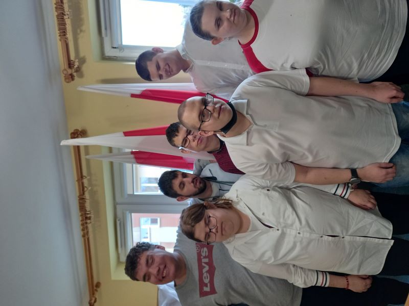 Zdjęcie grupowe uczniów Szkoły Przysposabiającej do Pracy. Na tle flagi Polski stoją Ola, Adam, Natalia, Adam, Adrian, Kuba, Maksymilian