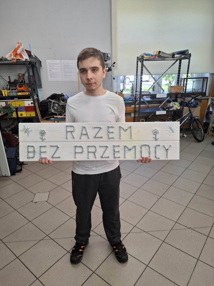 Uczeń klasy II M w pracowni mechanicznej prezentuje przygotowaną pracę- na drewnianej tablicy widnieje napis wykonany ze śrubek: „Razem bez przemocy”
