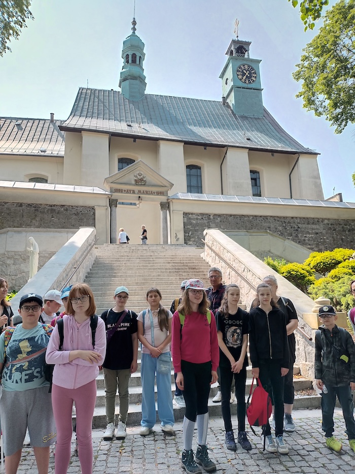 Uczestnicy wycieczki na schodach prowadzących do sanktuarium św. Anny na Górze Św. Anny, w tle wieże kościoła 